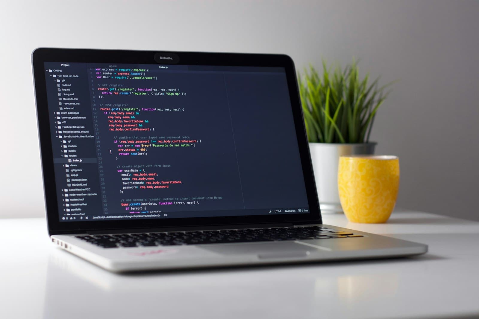Laptop on a white desk displaying program code in a dark-themed editor