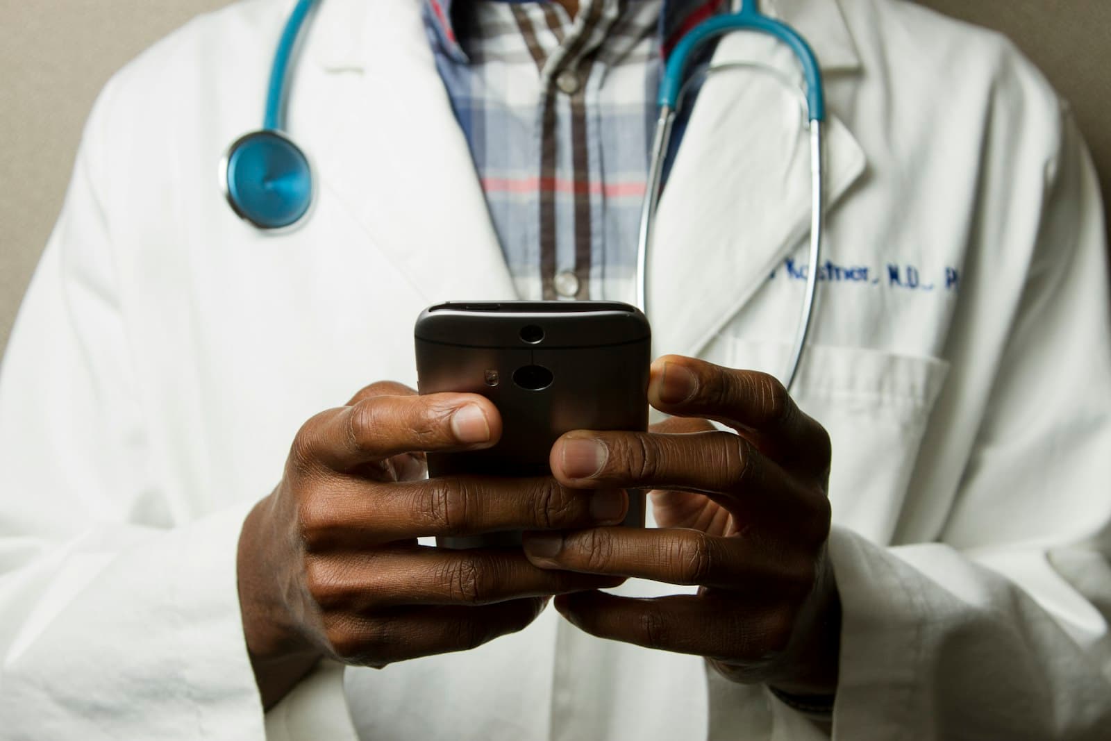 Healthcare professional in a white coat with a stethoscope reviewing information on a phone