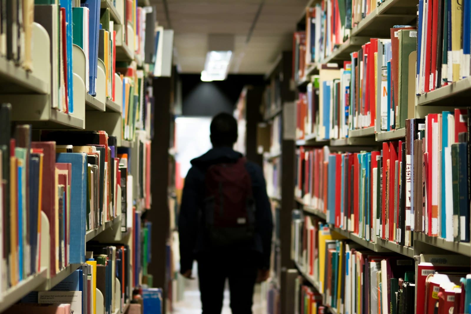 Student with a backpack walking between tall shelves of a university library